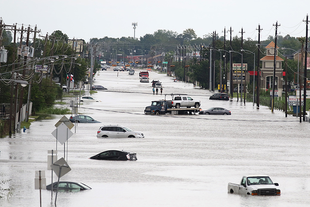 A car gets towed while men walk in floodwaters on a road in Houston, August 2017, in the wake of Hurricane Harvey. (Getty/Thomas B. Shea/AFP)