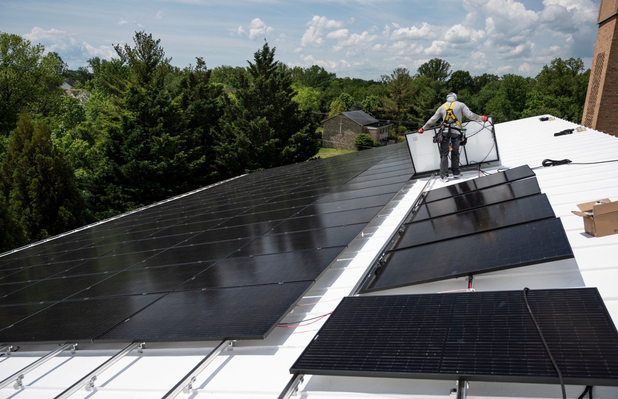 An employee with Ipsun Solar installs solar panels on the roof of the Peace Lutheran Church in Alexandria, Virginia on May 17, 2021. - Using donations, the church installed a 60.48 kilowatt solar instillation to bring down their carbon footprint. US President Joe Biden has called for the US energy sector to be fully decarbonized by 2035. To this end, he has asked Congress for $100 billion to invest in the national grid and shift to cleaner energy, as well as a ten-year extension of tax credits for renewable generation and storage. 