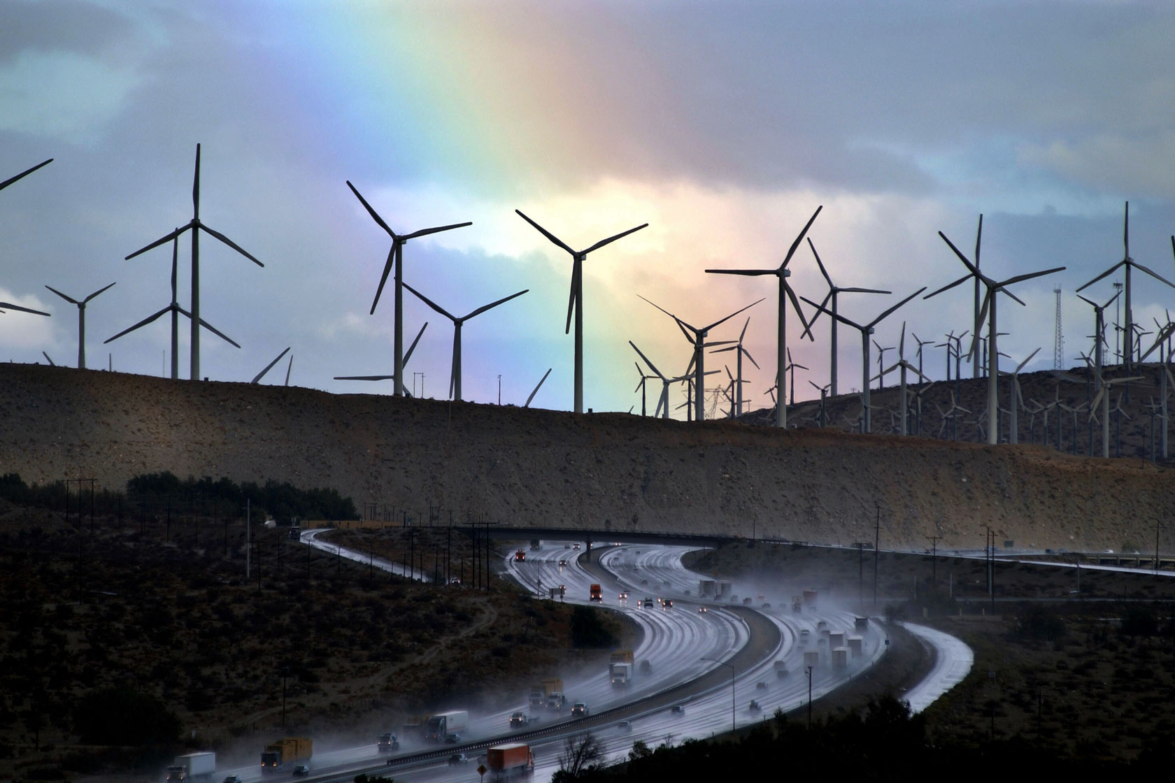 A rainbow forms behind windmills.