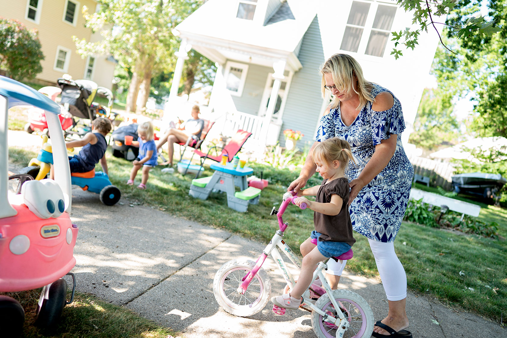 Photo shows a woman guiding a young girl on a bike.