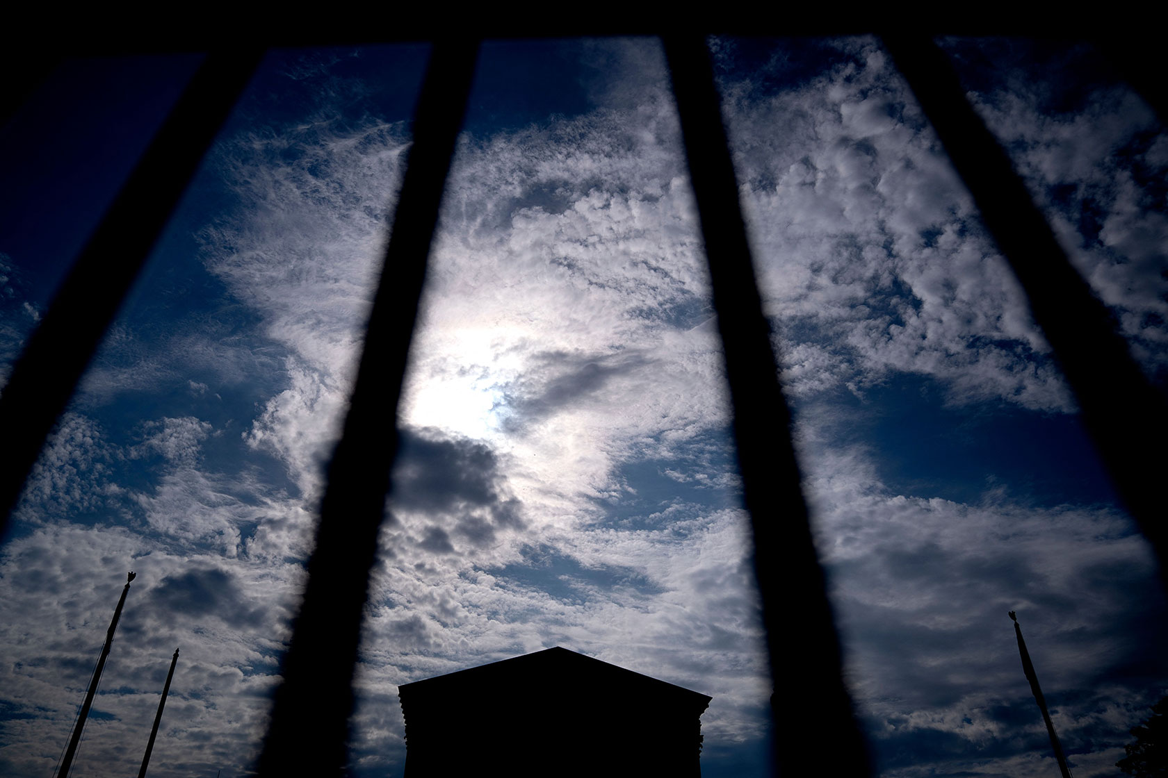 Photo shows the top of the U.S. Supreme Court building set against a dramatic sky, with the rails of a barricade in the foreground.