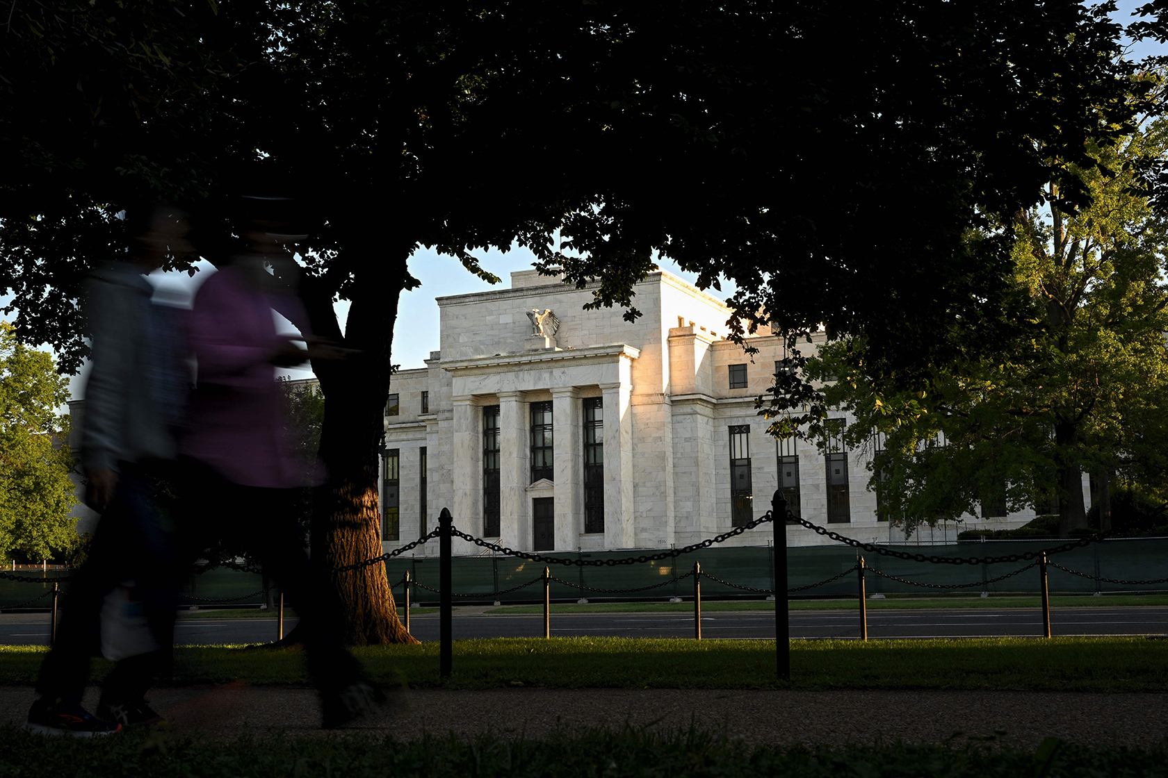 People, blurred, walking past the Federal Reserve building, which is in focus