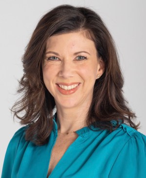 Photo shows Andrea Palmer smiling for a headshot, wearing a blue blouse