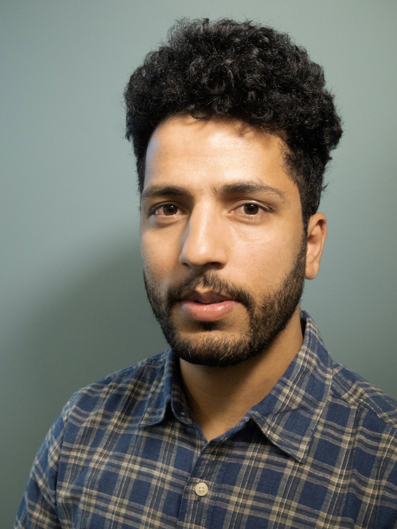 Raqib Naik headshot. Raqib is a Kashmiri man with short hair and wearing a plaid shirt.