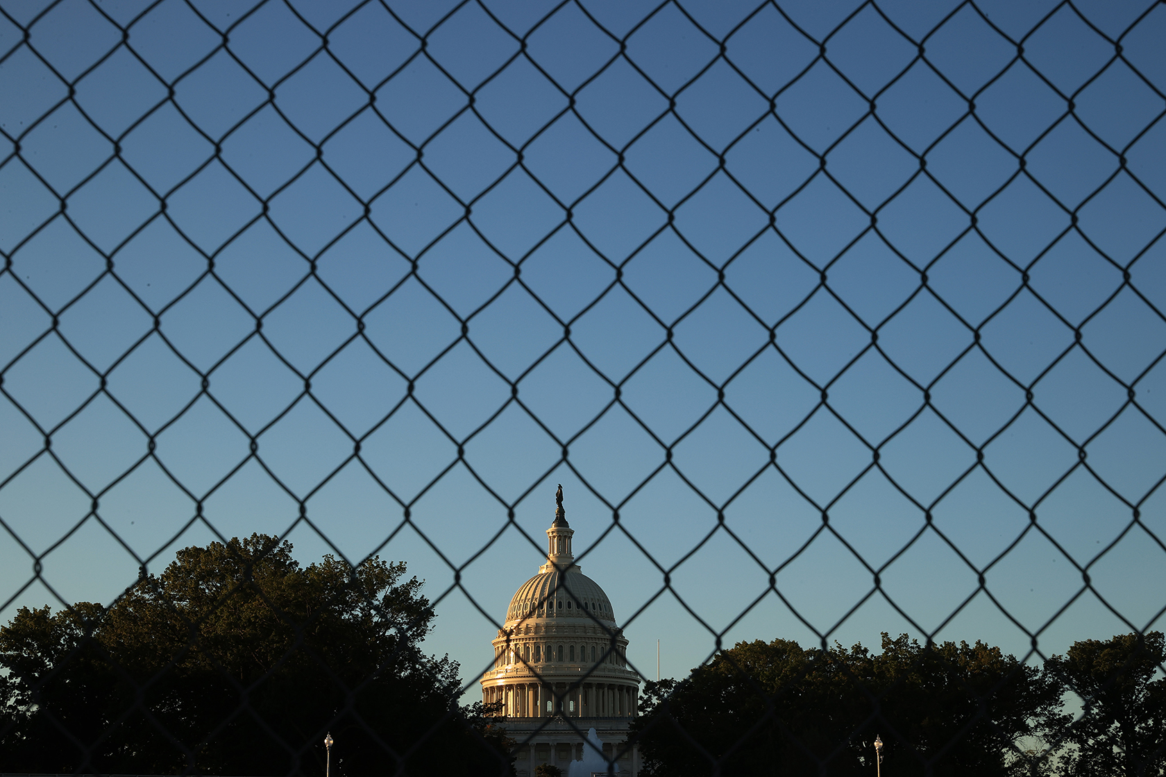 Capitol dome at sunrise, seen through chain-link fencing