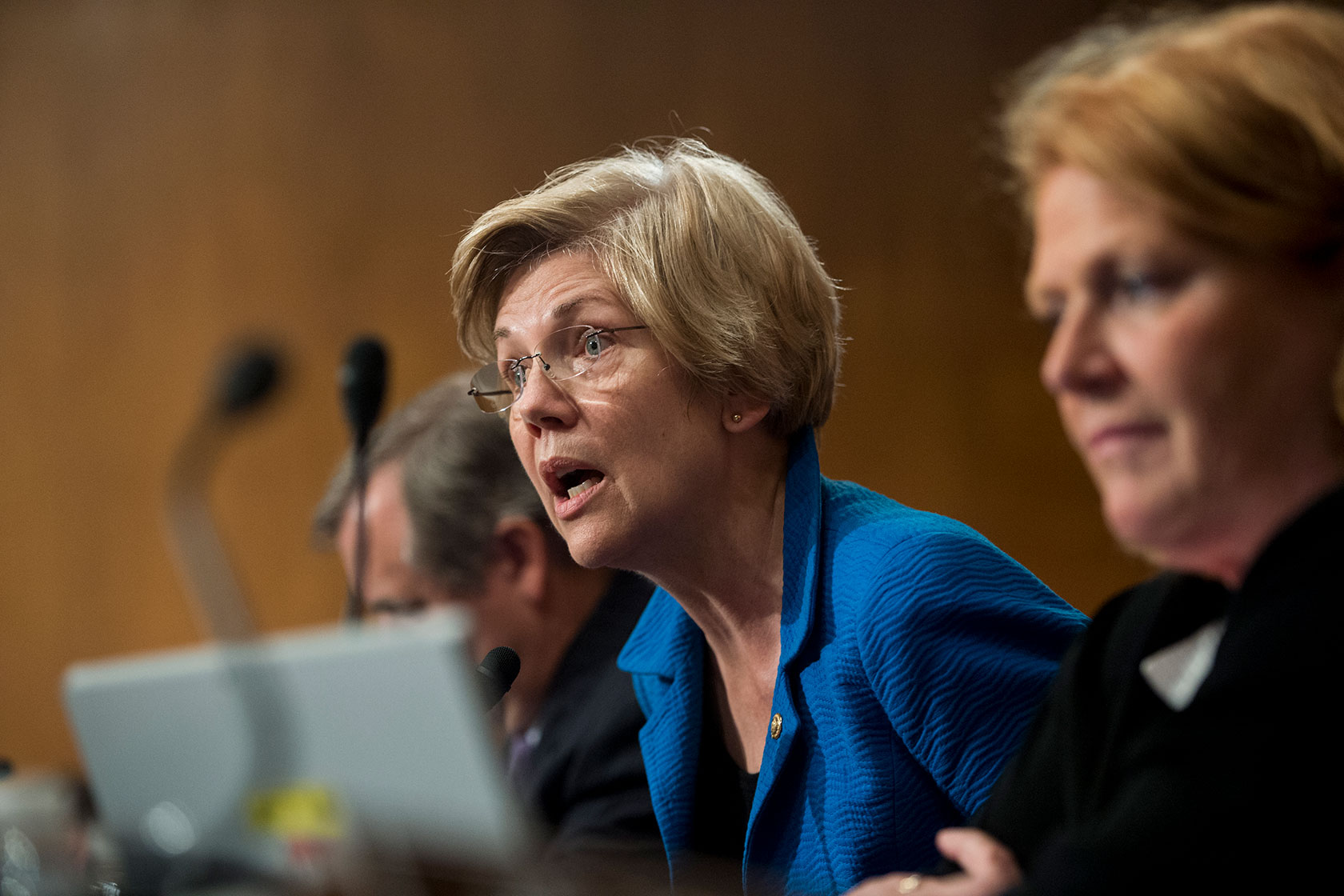 Photo shows Elizabeth Warren wearing a blue top speaking into a microphone