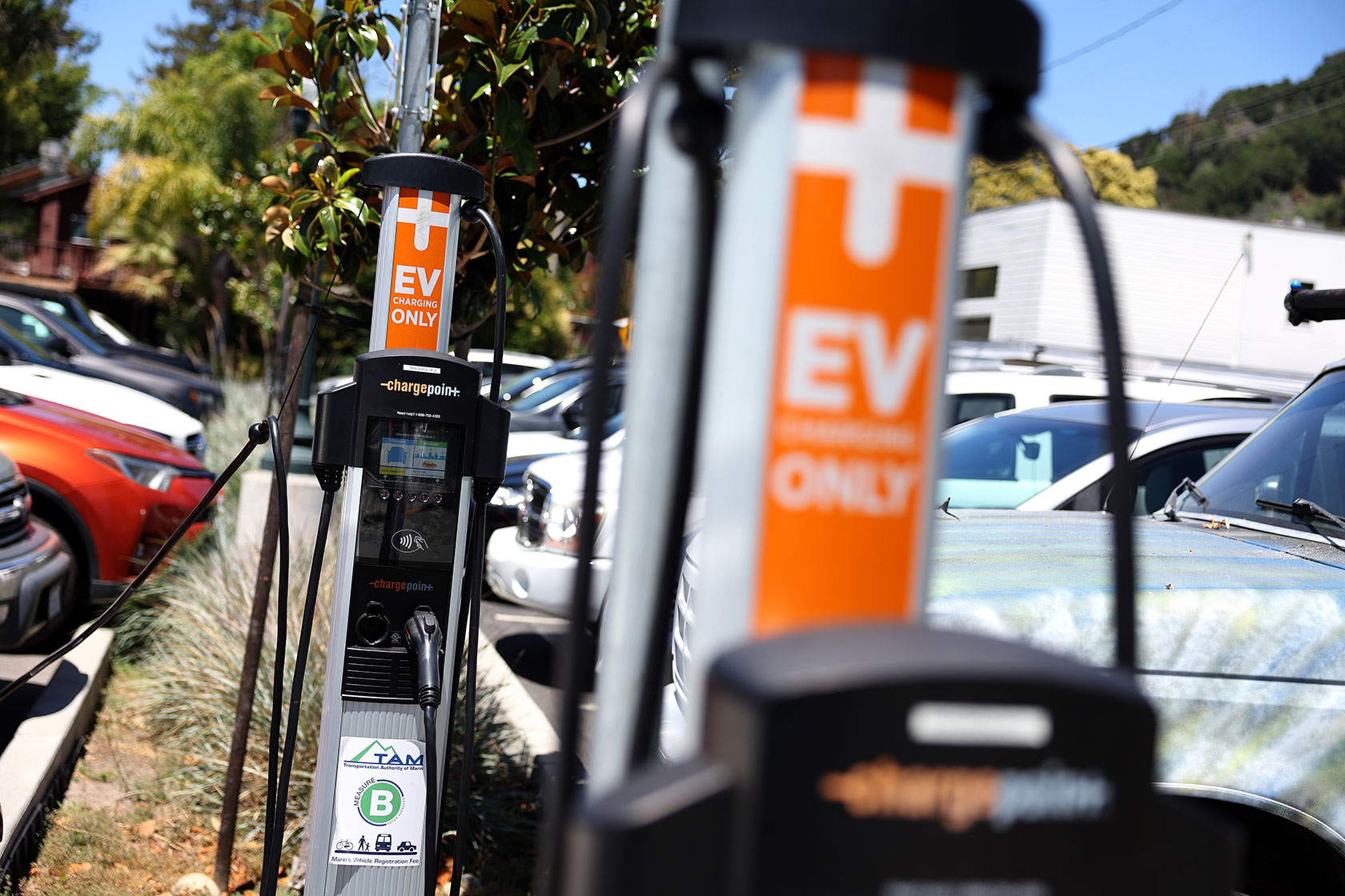 Photo shows several cars lined up on both sides of a divider with EV chargers that display orange signs reading 