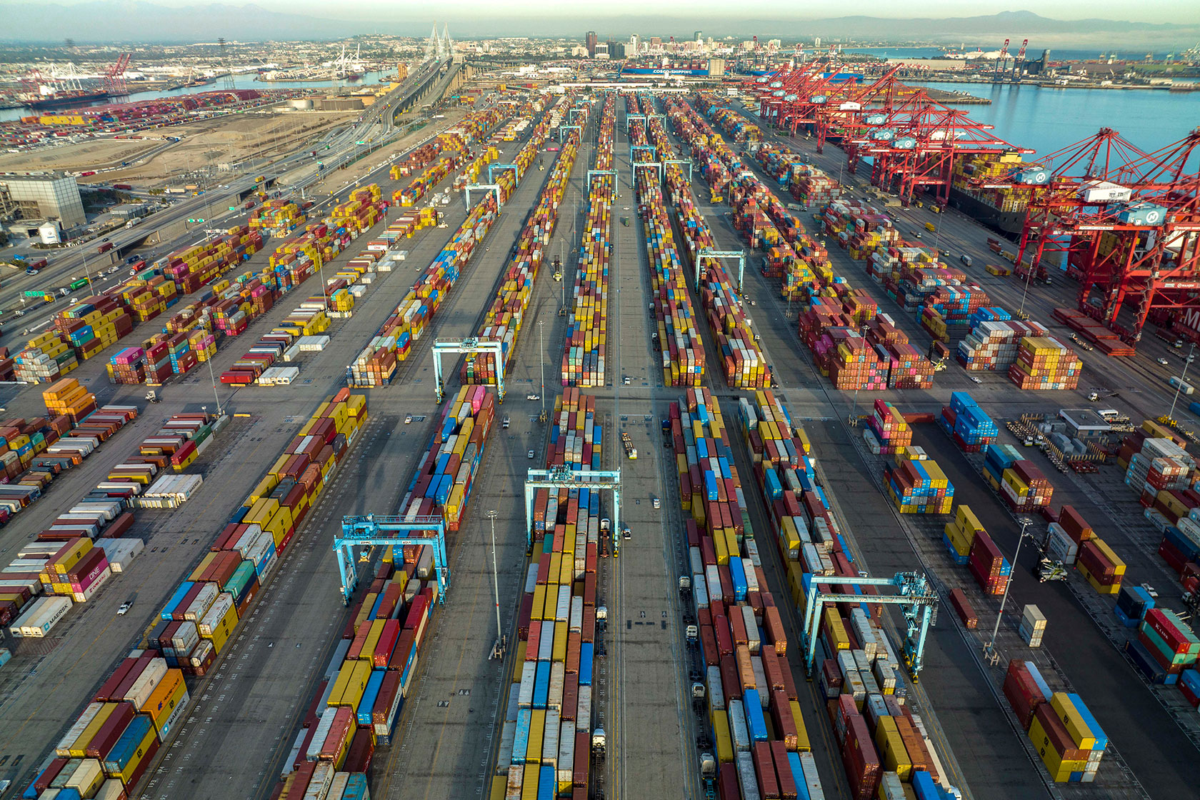 Photo shows several long rows of colorful shipping containers against a smoggy blue sky