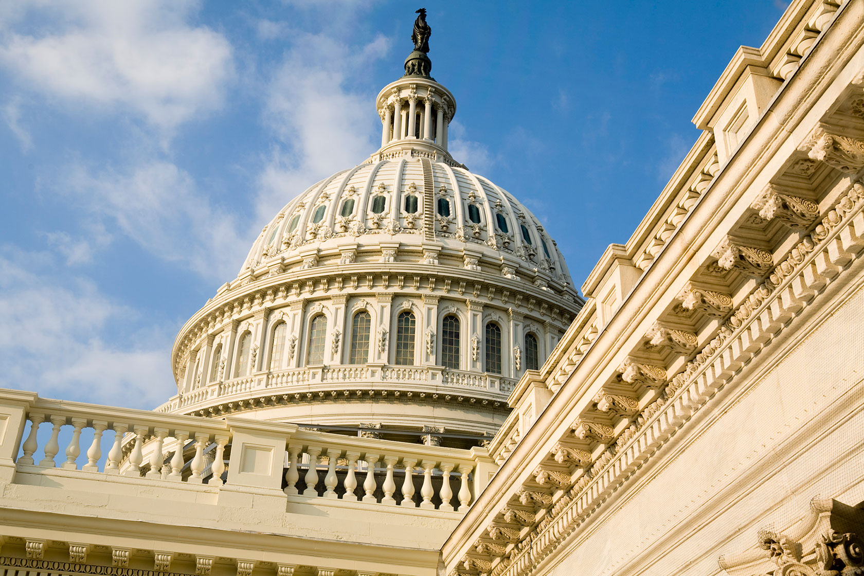 Photo shows a closeup of the Capitol building dome against a mostly blue sky