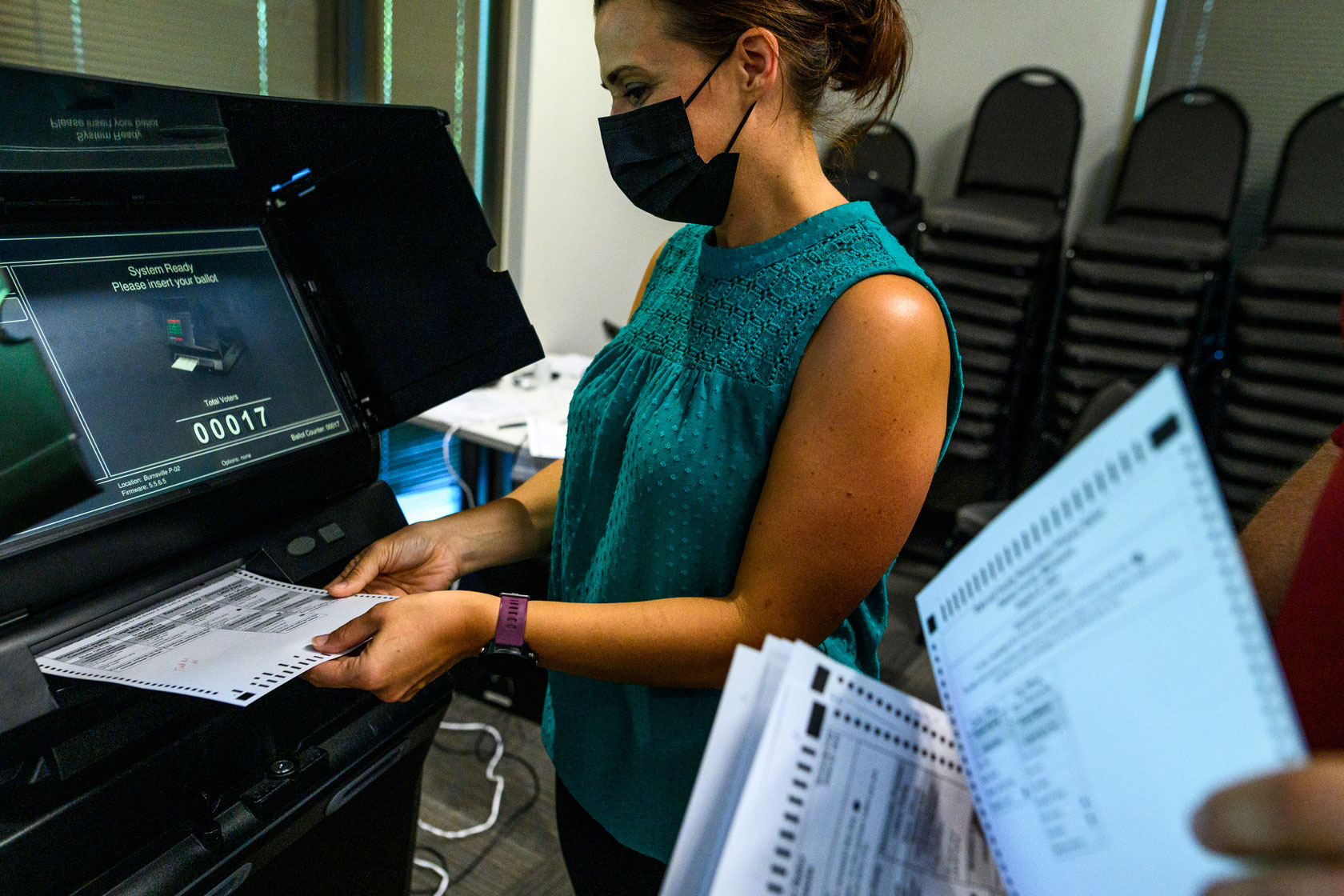 Photo shows someone sliding a paper ballot into an electronic ballot scanner.