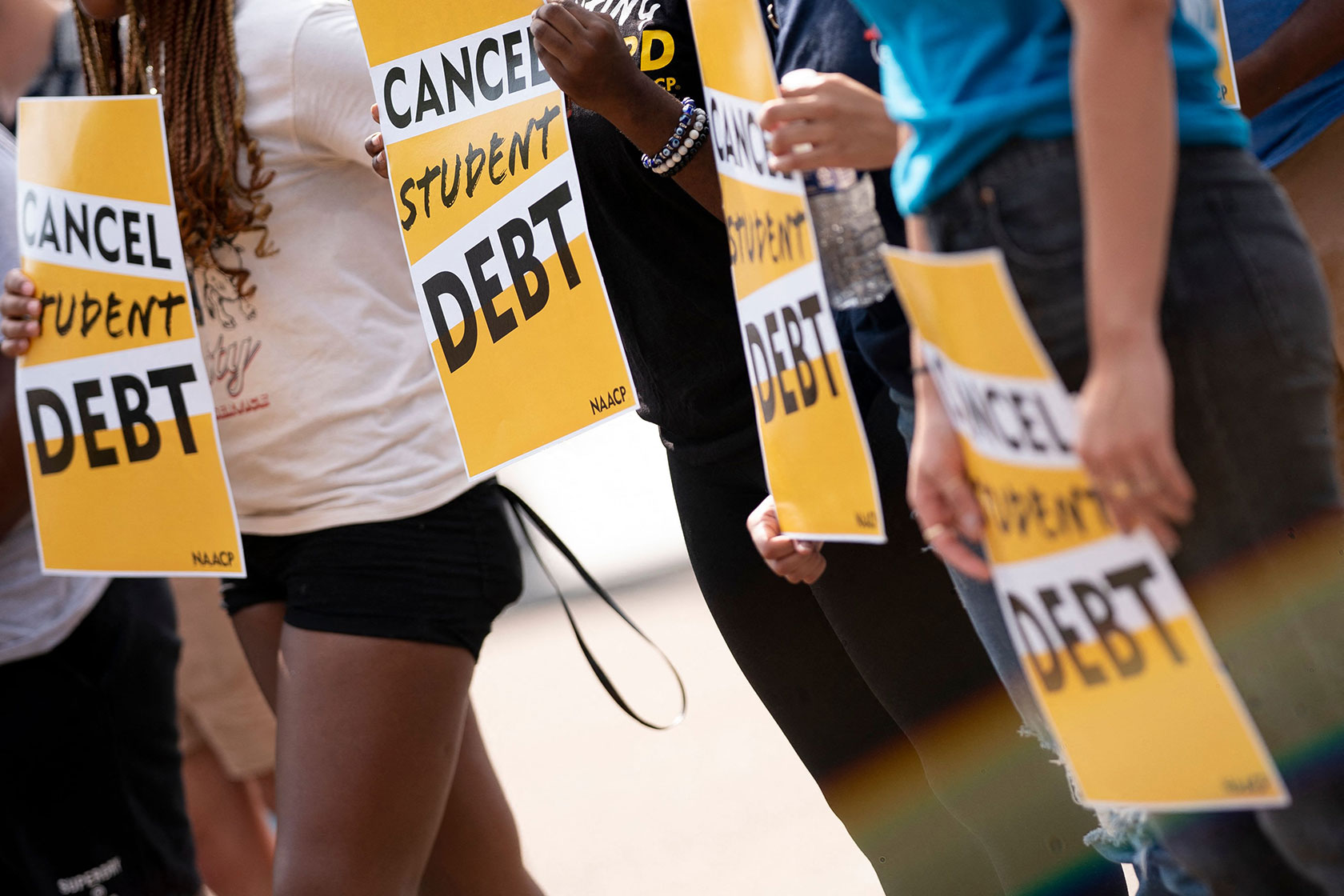 Photo shows a lower view of a few people holding yellow signs that read 
