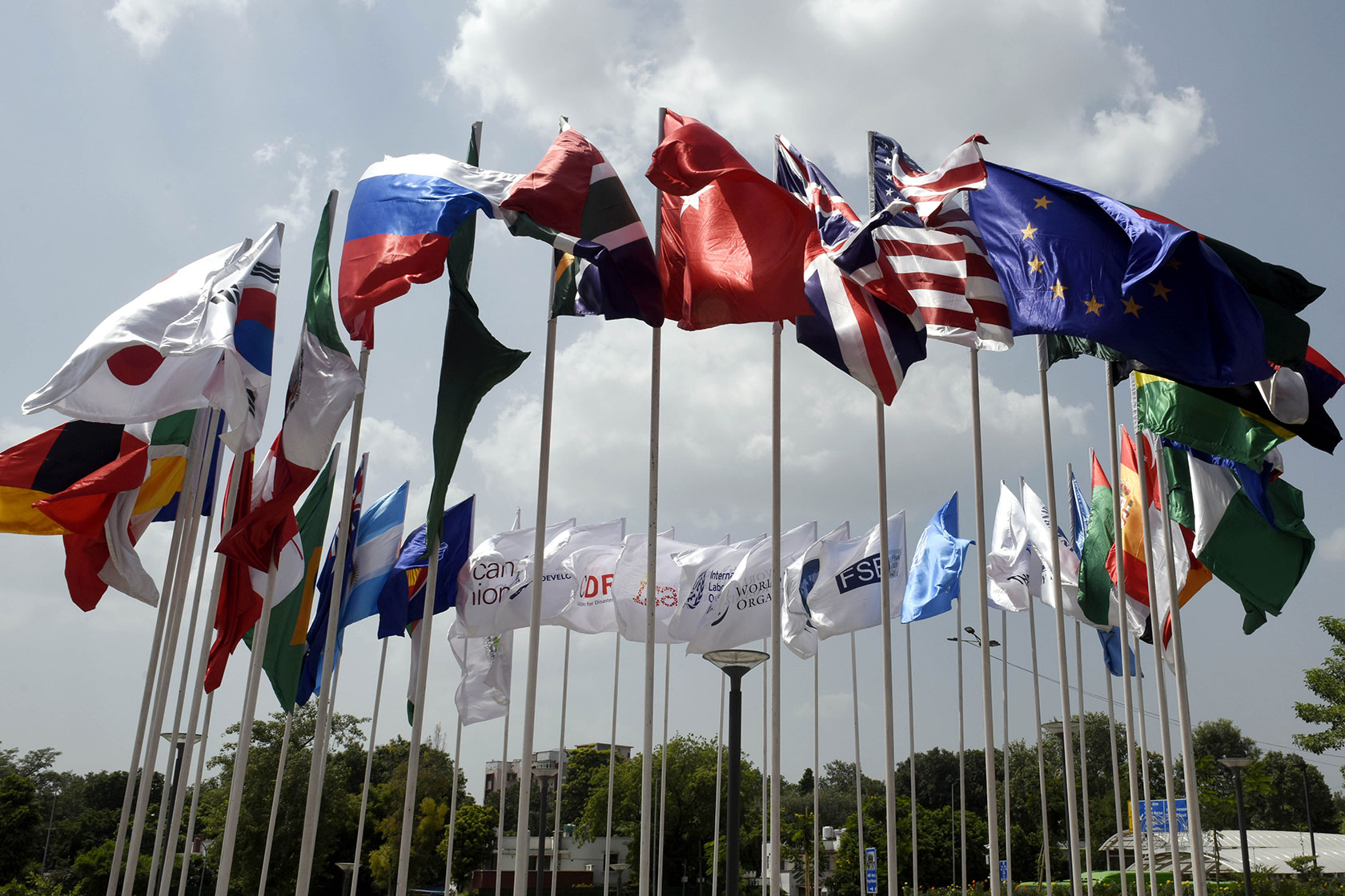Photo shows several flags arranged in a circular formation, flying against a grey cloudy sky
