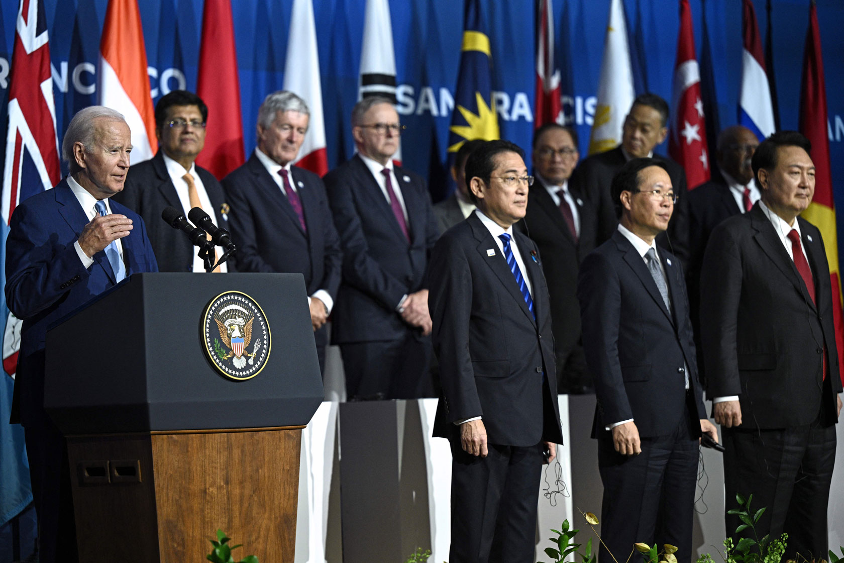 President Joe Biden speaks from behind a podium next to other IPEF leaders with country flags in the background.
