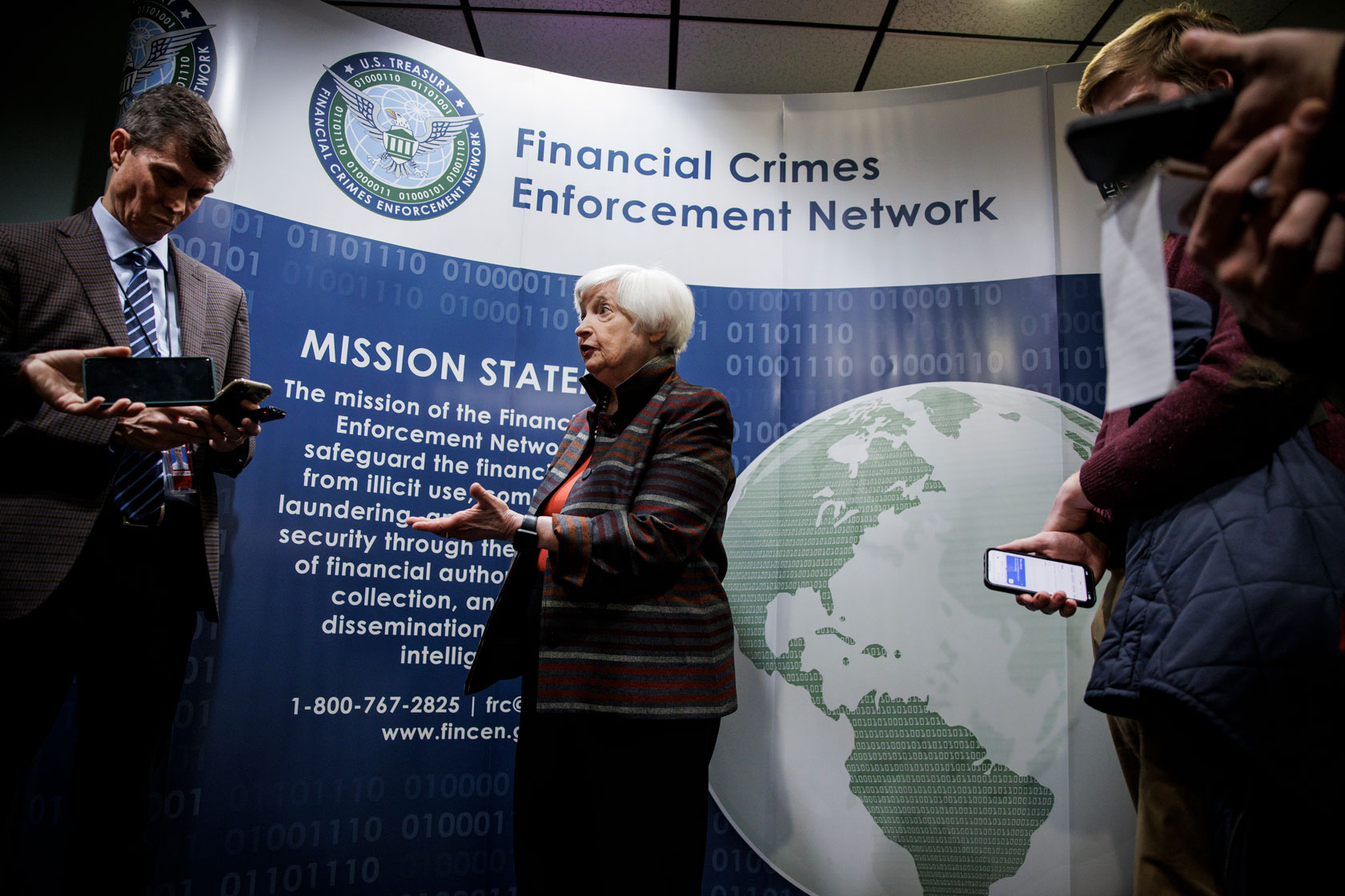U.S. Secretary of the Treasury is seen in front of a sign surrounded by reporters.