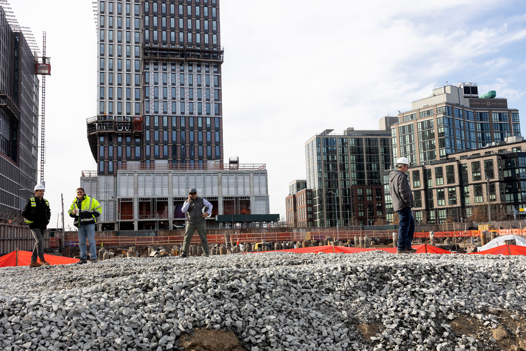 Construction workers are seen on-site with large apartment buildings in the background.