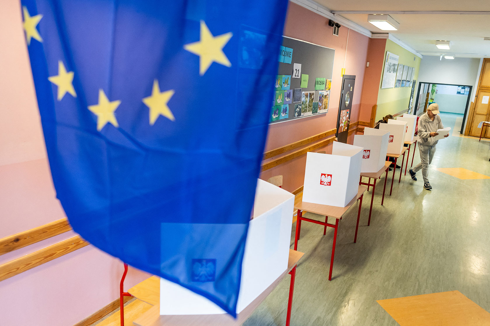Photo shows the EU flag displayed in the foreground, and one man near polling stations in an empty hallways